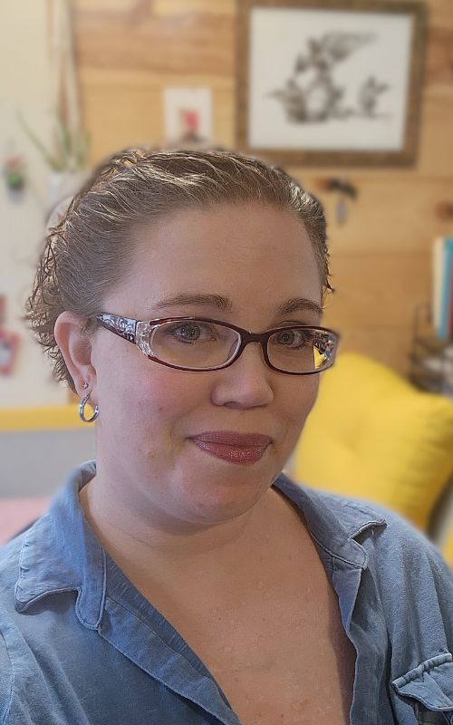 Woman with short curly hair and red glasses, smiling at the camera.